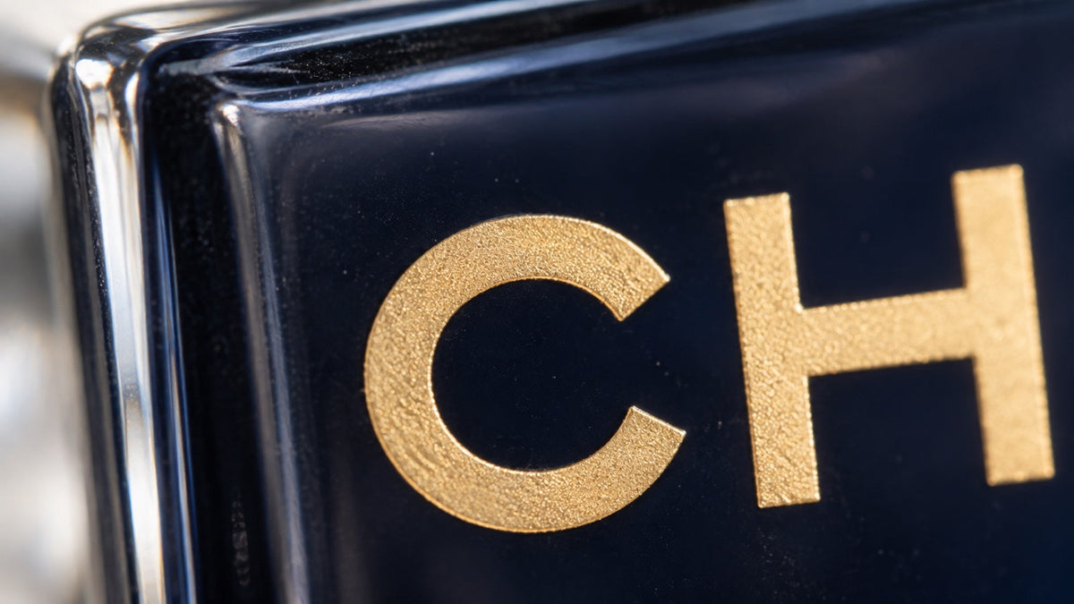 Ultramakroaufnahme goldener Schrift auf dunkelblauem Glas eines Bleu de Chanel Flakons.